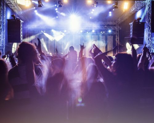 Rear view of a concert crowd with parts of the stage visible. Psychedelic colors.